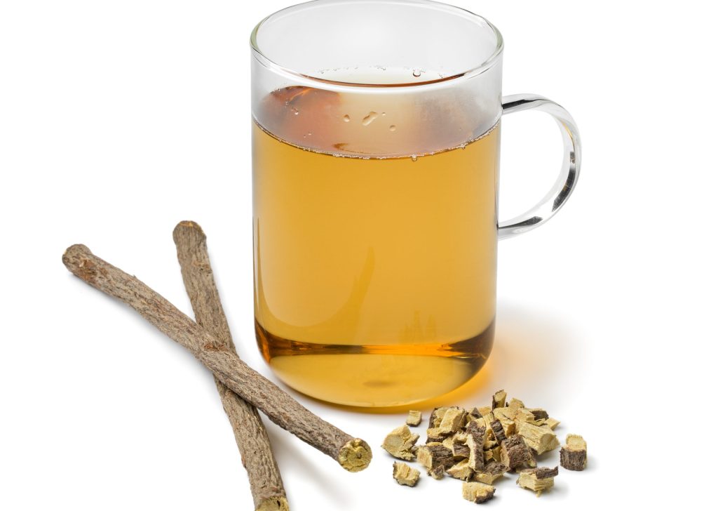 Glass of licorice tea and pieces of roots isolated on white background